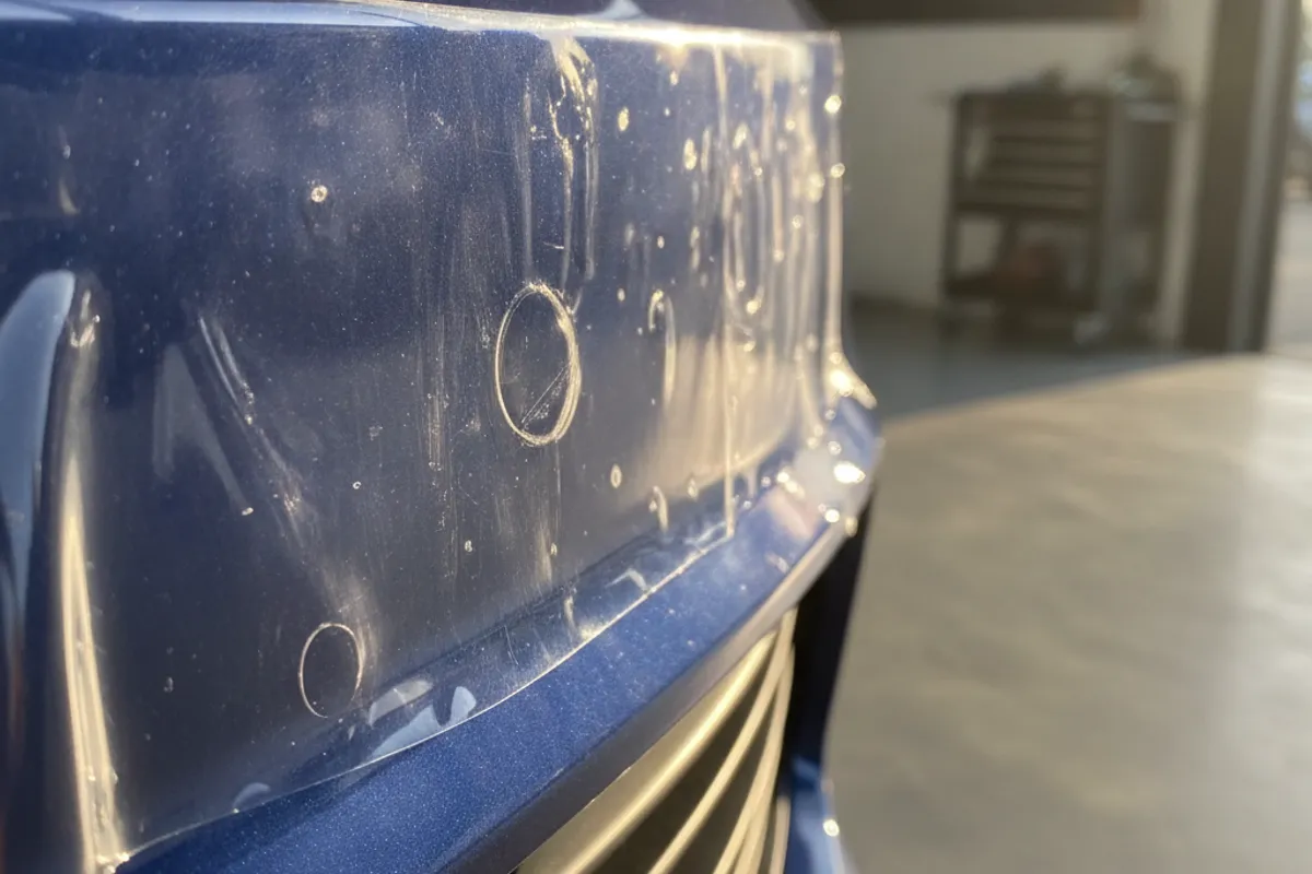 Close-up of a car's front bumper with paint protection film being carefully applied by a technician
